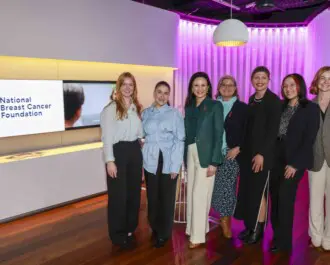 Seven people from the National Breast Cancer Foundation (NBCF) Team smiling next to the NBCF logo